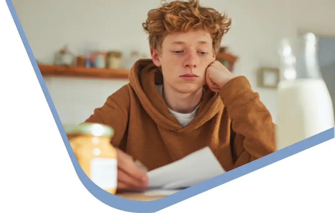 504 Accommodation-optimized Teenager reading documents at the kitchen table, with a jar of peanut butter and a bottle of milk nearby.